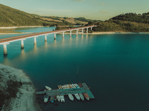 Aerial view of the bridge spanning Lago di Castreccioni with small boats moored at a wooden dock in Cingoli, Marche, Italy.