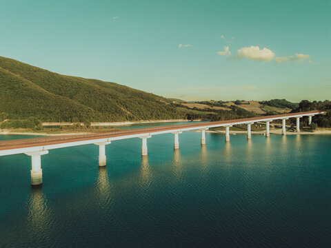 Aerial view of the bridge crossing Lago Castreccioni surrounded by green hills and calm water in Cingoli, Marche, Italy.