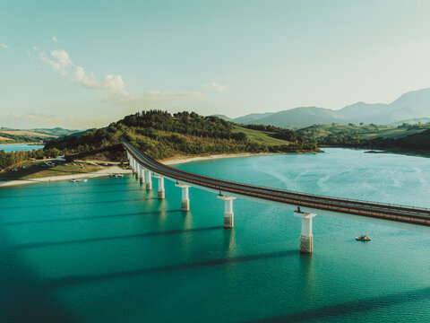 Aerial view of the bridge over Lago Castreccioni, surrounded by rolling hills and lush greenery in Cingoli, Marche, Italy.