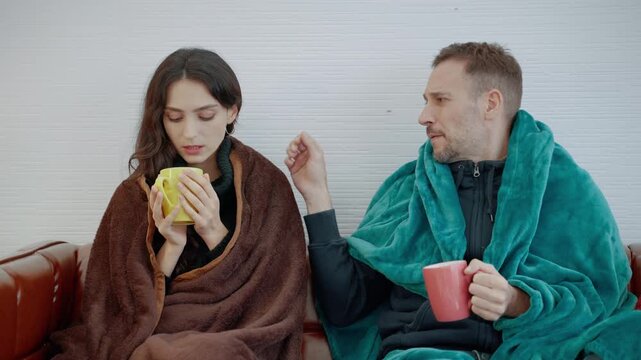Couple wrapped in warm blankets and drinking hot beverages while relaxing together on a sofa during a cold winter day at home.
