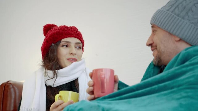 Happy couple wearing warm winter clothing and smiling at each other while enjoying a cozy moment together at home.

