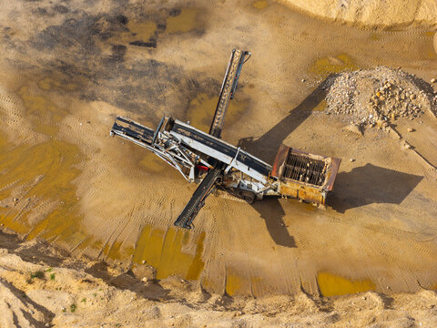 Aerial view of asphalt production machinery at a road construction plant with conveyor belts and piles of sand and gravel in Poland.