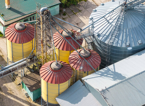 Aerial view of a grain elevator facility featuring yellow and red silos, a large metal storage tank, and industrial structures on a concrete site in Poland.