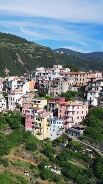Picturesque aerial view of a coastal Corniglia village in Cinque Terre, Italy, with church and colorful hillside houses surrounded by lush greenery and overlooking the serene Mediterranean Sea