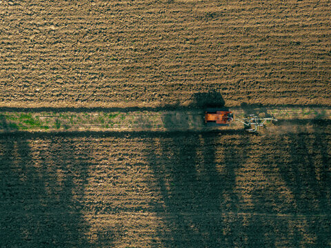 Aerial view of a tractor working in a large, plowed agricultural field in Osteria di Colleponi, Marche, Italy.