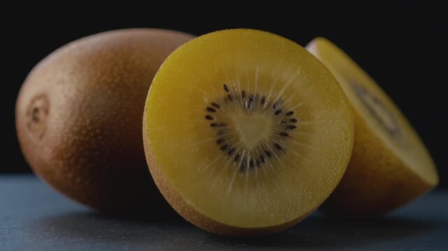 Macro shot of a ripe golden kiwi cut in half with a heart-shaped core, rich juicy pulp and seeds on a dark background with a blurred whole kiwi for healthy eating, gourmet food, and culinary content.