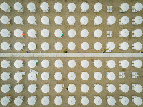 Aerial view of rows of white beach umbrellas and sun loungers arranged on the sandy beach in San Benedetto del Tronto, Marche, Italy.