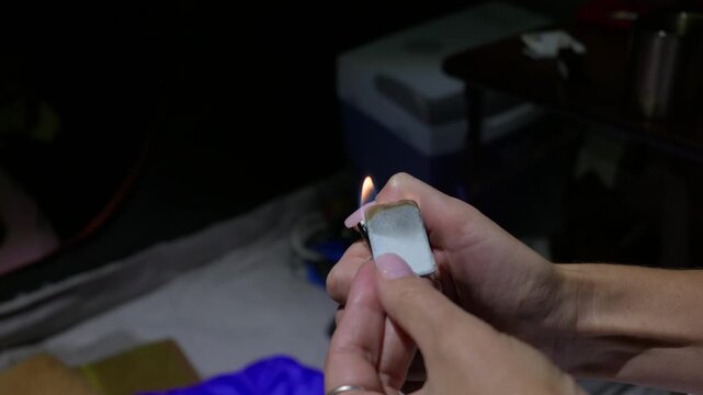 Hands ignite a fumigation repellent tablet with a small flame in a dark outdoor setting. The practical sequence supports camping safety demonstrations and night survival guides.