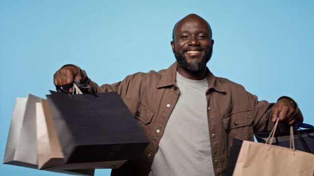 Portrait of happy African American man holding shopping bags, turning around and smiling. Video suitable for retail marketing, seasonal sales and consumer discount advertising