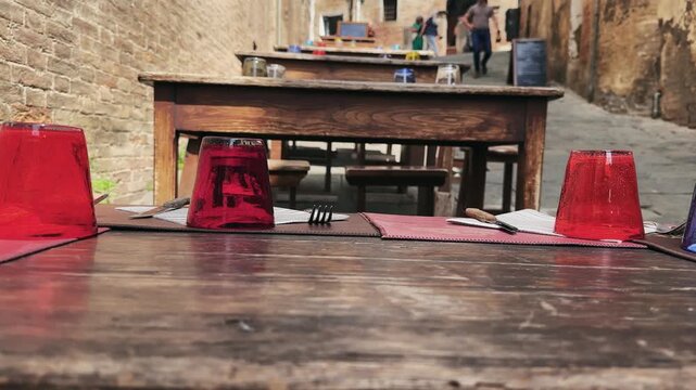 Charming street restaurant in Siena, Tuscany with wooden tables adorned with colorful glasses
