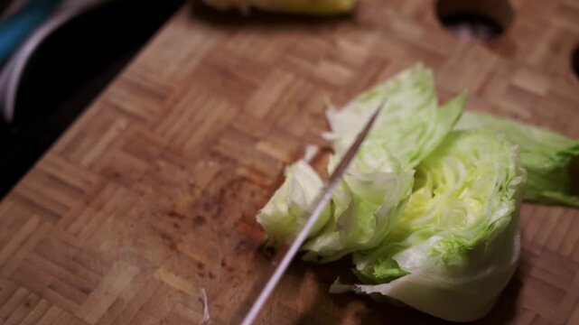 Cutting lettuce head with knife on wooden cutting board. Woman cutting fresh lettuce.