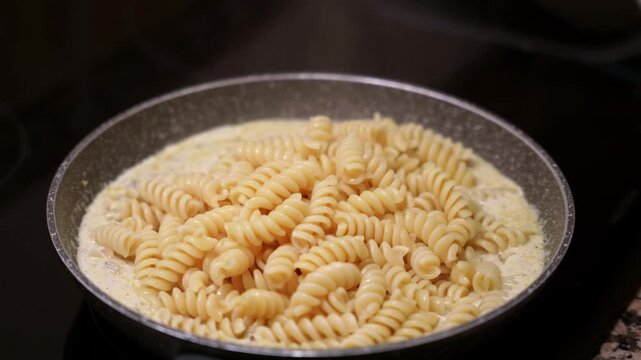 Fusilli pasta cooking in creamy mushroom sauce in pan. Close up of creamy fusilli dish with mushroom sauce.