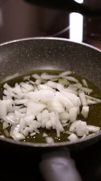 Putting diced onion in frying pan with olive oil. Cooking at home.