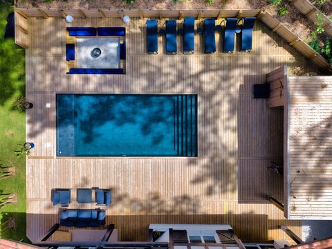 Aerial view of a modern swimming pool with a wooden deck, lounge chairs, and an outdoor seating area in Hossegor, Nouvelle-Aquitaine, France.