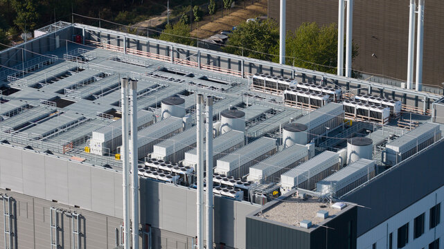 Aerial view of the industrial rooftop featuring numerous HVAC cooling units, ventilation systems, and tall chimneys on a modern building in Frankfurt am Main, Hessen, Germany.