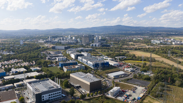 Aerial view of industrial and commercial buildings surrounded by green spaces and trees with the city skyline in the distance in Frankfurt am Main, Hessen, Germany.