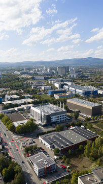 Aerial view of industrial and commercial buildings with solar panels on rooftops, surrounded by trees and roads in Frankfurt am Main, Hessen, Germany.
