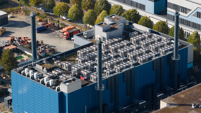 Aerial view of a large industrial facility featuring a blue facade, numerous rooftop HVAC units, and tall chimneys in an industrial area in Frankfurt am Main, Hessen, Germany.