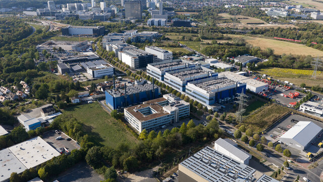 Aerial view of modern industrial and business park buildings with large rooftops, surrounding green spaces, and infrastructure in Frankfurt am Main, Hessen, Germany.