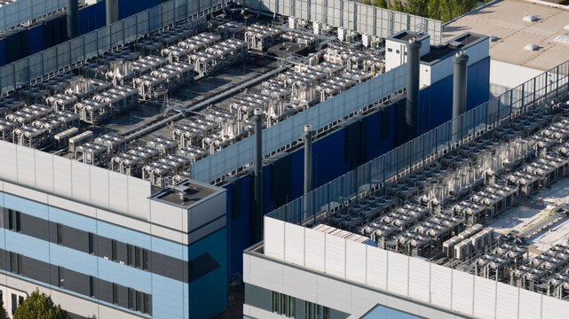 Aerial view of a large industrial data center rooftop featuring rows of cooling units and HVAC systems, set against a modern blue and grey building facade in Frankfurt am Main, Hessen, Germany.