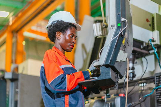 African woman machine operator inspecting metal part at CNC machine in automotive parts factory