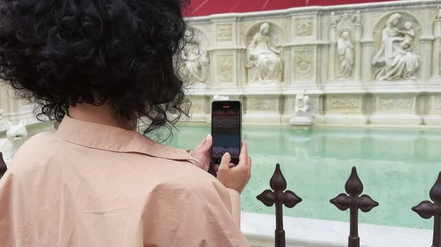 Woman tourist capturing video of a historic fountain Fontana della Birretta in Siena, Tuscany