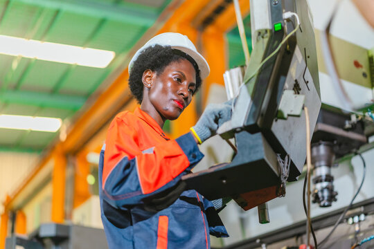African woman machine operator inspecting metal part at CNC machine in automotive parts factory