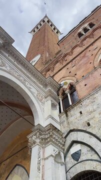 Torre del Mangia tower in Siena, Tuscany, stands majestically against a cloudy sky, vertical video