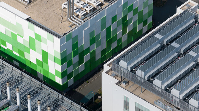 Aerial view of a modern data center facility featuring a distinctive green and white checkered facade, rooftop cooling units, and industrial infrastructure in Frankfurt am Main, Hessen, Germany.