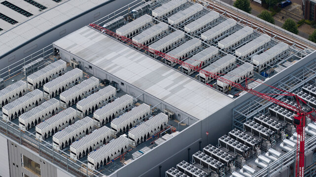 Aerial view of a large industrial building roof featuring numerous HVAC cooling units and a red construction crane in Slough, England, United Kingdom.