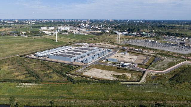 Aerial view of a large industrial power facility with solar panels on the roof, surrounded by green fields and power lines in Groningen, Groningen, Netherlands.