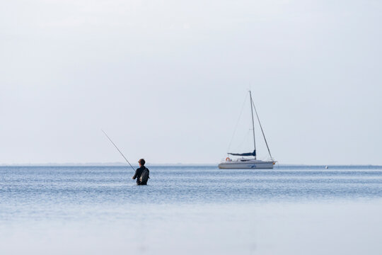 Pescador en la playa un amanecer con barco de fondo y el mar en calma