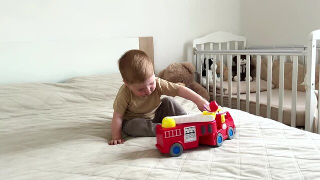 Two year old boy playing with small cars on bed. Racing and parking toy vehicles. Fine motor skills through push and go play. Classic boyish toy fun
