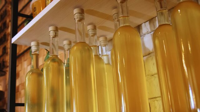 Corked glass bottle of yellow liquid on wooden shelf low angle shot. Delicious syrup white wine and oil collection in cafe kitchen closeup