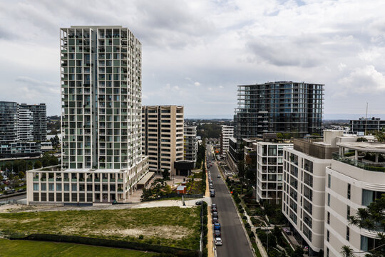 Aerial view of modern high-rise apartment buildings and mixed-use developments forming an urban street canyon with parked cars along the road in Norwest, New South Wales, Australia.