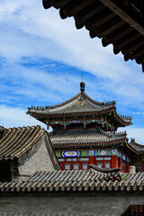Fototapeta premium Framed view of an ornate multi-tiered ancient Chinese pavilion, vibrant painted dougong brackets, grey tiled roofs, bright blue sky with wispy clouds.