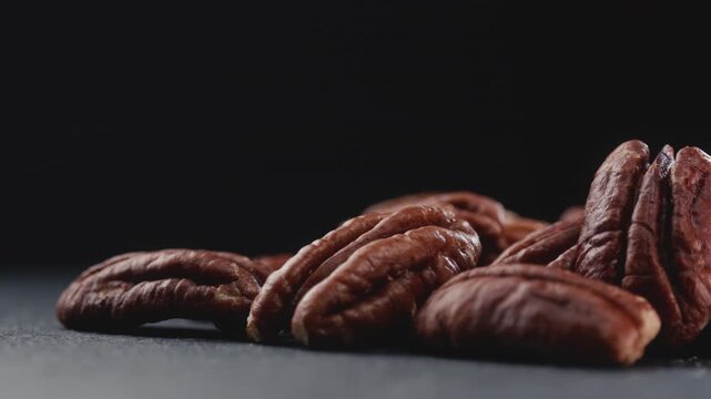 Extreme macro shot of fresh premium pecan nuts with selective focus, rotating slowly on dark background with artistic lighting. Perfect for healthy eating, gourmet food, culinary, and dietary content.