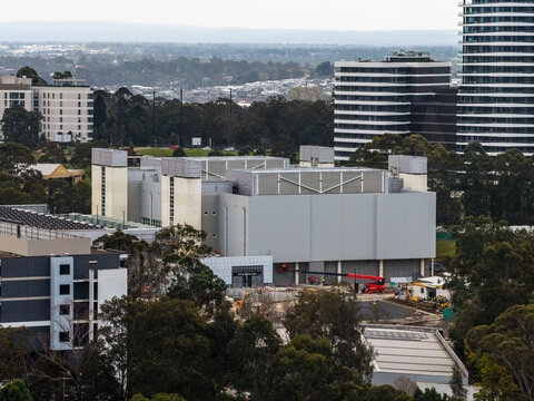 Aerial view of a data centre facility under construction with cranes and machinery, surrounded by modern office buildings and trees in Norwest, New South Wales, Australia.