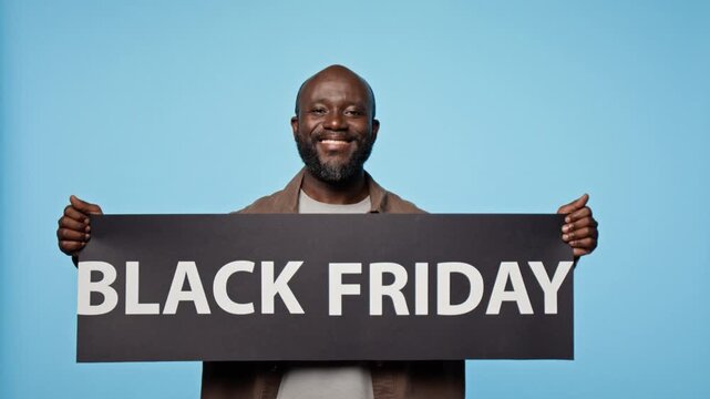 Portrait of African American man raising Black Friday banner while smiling at camera. Visual suitable for retail sale promos, seasonal discounts and holiday ecommerce campaigns
