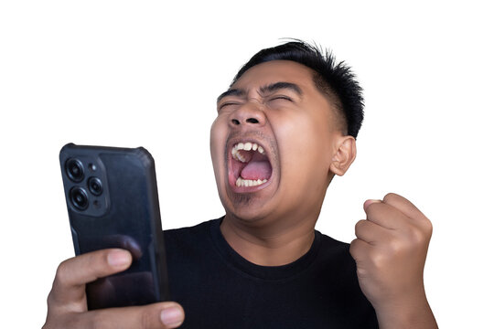Overjoyed and ecstatic Indonesian man wearing a black t-shirt looking at his mobile phone while pumping his fist and screaming loudly in celebration against a white background.