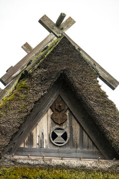Close-up of a thatched gable apex with crossed wooden ridge timbers above a carved floral ornament and circular crest symbol, Kyoto prefecture, Miyama, Japan