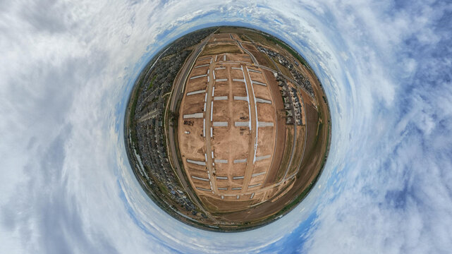Aerial view of a residential construction site with earthworks and concrete foundations surrounded by suburban housing in a 360-degree panoramic perspective in Longmont, Colorado, United States.