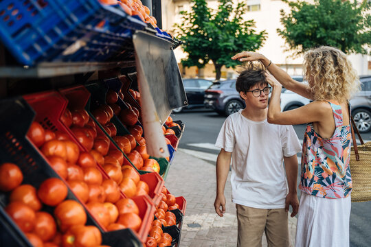 Caring mature mother helping teenage son with Down syndrome during outdoor market shopping in Spain