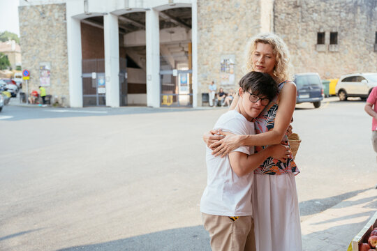 Loving mature mother embracing teenage son with Down syndrome after shopping at local market