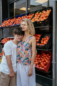 Caring mature mother standing with teenage son with Down syndrome beside fresh tomato market display
