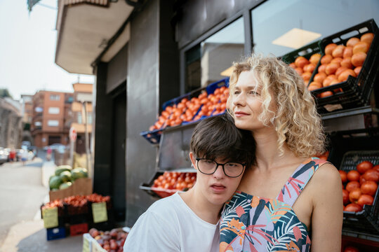 Caring mature mother standing close with teenage son with Down syndrome beside local market