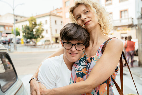 Caring mature mother hugging teenage son with Down syndrome during everyday city walk