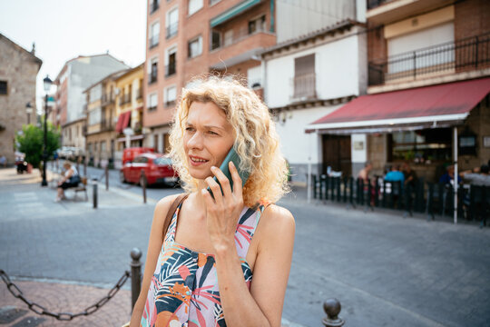Mature woman talking on smartphone in sunny Spanish town square during summer day