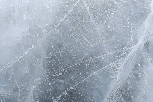Frozen ice surface with delicate natural cracks and trapped air bubbles, creating a cool, clean, and minimalist texture in neutral tones.