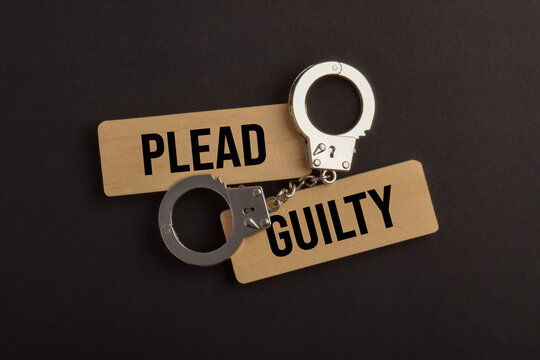 Handcuffs placed over wooden signs labeled Lead and Guilty, representing criminal responsibility, legal charges, prosecution, law enforcement, and justice.